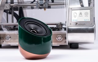 A small green speaker sat infront of a 3D printer
